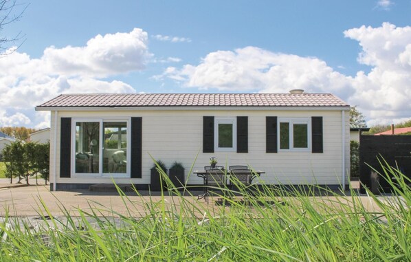 Ein eingeschossiges Haus mit Ziegeldach, großen Fenstern mit Fensterläden und einer Terrasse mit Tisch und Stühlen.