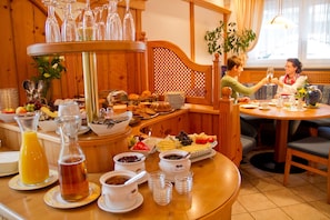 A breakfast buffet with various food items and beverages, wooden furniture, and a window with natural light.