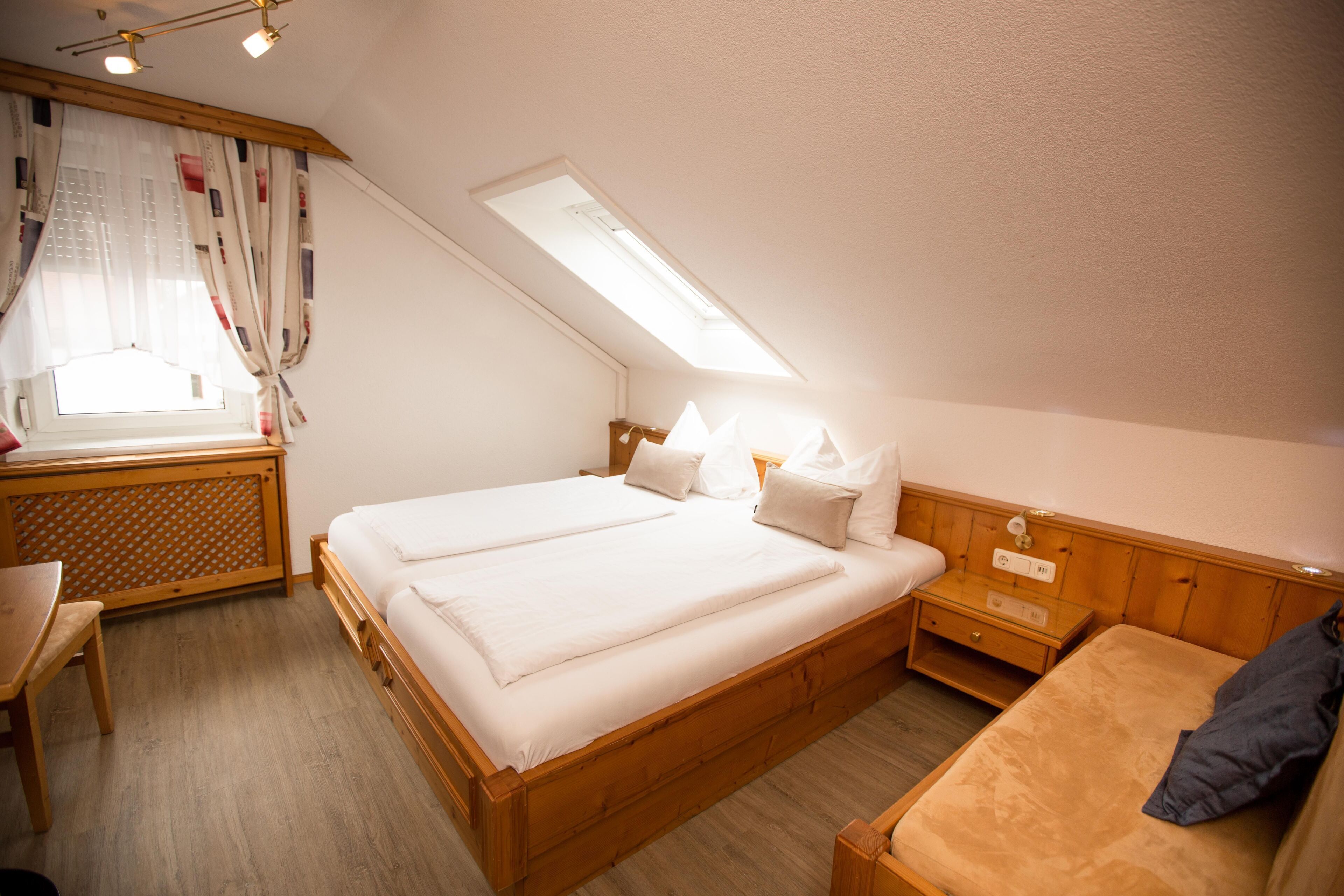 Une chambre avec deux lits, un bureau, une chaise, une table de chevet et une fenêtre avec des rideaux.
