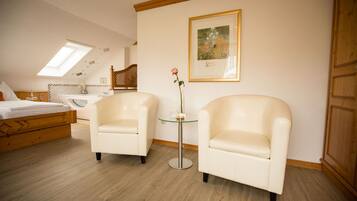 Une chambre à coucher avec un lit, deux fauteuils, une petite table sur laquelle est posé un vase, un tableau encadré au mur et une armoire en bois.