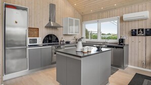 A modern kitchen with a central island, stainless steel appliances, and a large window providing a view of the outdoors. - Gorgeous home in Tarm with sauna (Tarm)