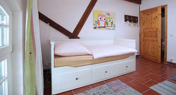 A bedroom with a white bed, a wooden ceiling, a wall-mounted artwork, and a wooden door.