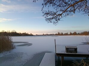 Un lago congelado con un muelle y un banco, rodeado de árboles y un cielo despejado.