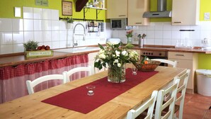 Une cuisine avec des meubles blancs, une table en bois surmontée d’un set de table rouge et un vase rempli de fleurs.