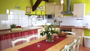 Eine Küche mit weißen Schränken, einem Holztisch mit einer roten Tischmatte und einem Blumenstrauß.