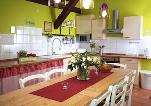 Eine Küche mit weißen Schränken, einem Holztisch mit einer roten Tischmatte und einem Blumenstrauß.