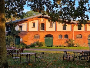 Un bâtiment en briques, doté de nombreuses fenêtres et de portes vertes, entouré d’une pelouse et agrémenté d’un espace de détente extérieur.
