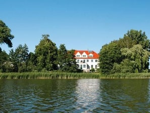 Ein Haus mit rotem Dach, umgeben von Bäumen und einem Gewässer.