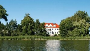 Une maison avec un toit rouge, entourée d’arbres et bordée par un plan d’eau.