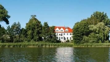 Ein Haus mit rotem Dach, umgeben von Bäumen und einem Gewässer.