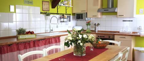 Una cocina con armarios blancos, una mesa de madera con un mantel individual rojo y un jarrón con flores.