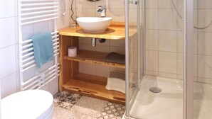 Une salle de bain avec un lavabo blanc, un miroir, un porte-serviettes et une douche.