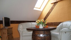 Een kamer met een witte leren bank, een houten vat-tafel en een televisie op een houten standaard.