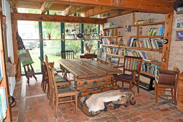 A rustic room with a wooden table, chairs, a bookshelf, and a large window.