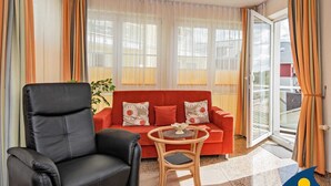 Ein Wohnzimmer mit einem schwarzen Ledersessel, einem roten Sofa mit floralen Kissen und einem kleinen runden Tisch mit einem Buch.