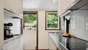 Ett kompakt kök med vita skåp, en kaffebryggare, en diskho och en fruktskål på bänkskivan.