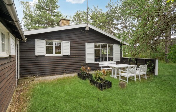 A small wooden house with two windows and a patio with a table and chairs.