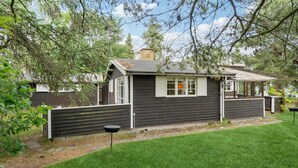 Ett litet, mörkt trähus med en inhägnad trädgård, en liten veranda och en synlig brevlåda.