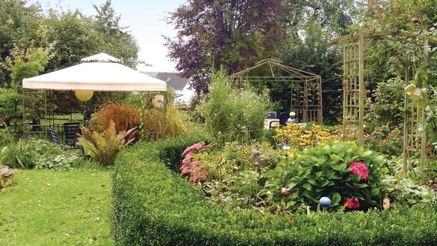 A well-maintained garden with a variety of plants and flowers, a wooden pergola, and a covered seating area. - 2 bedroom nice home in Schwalenberg (Schwalenberg)