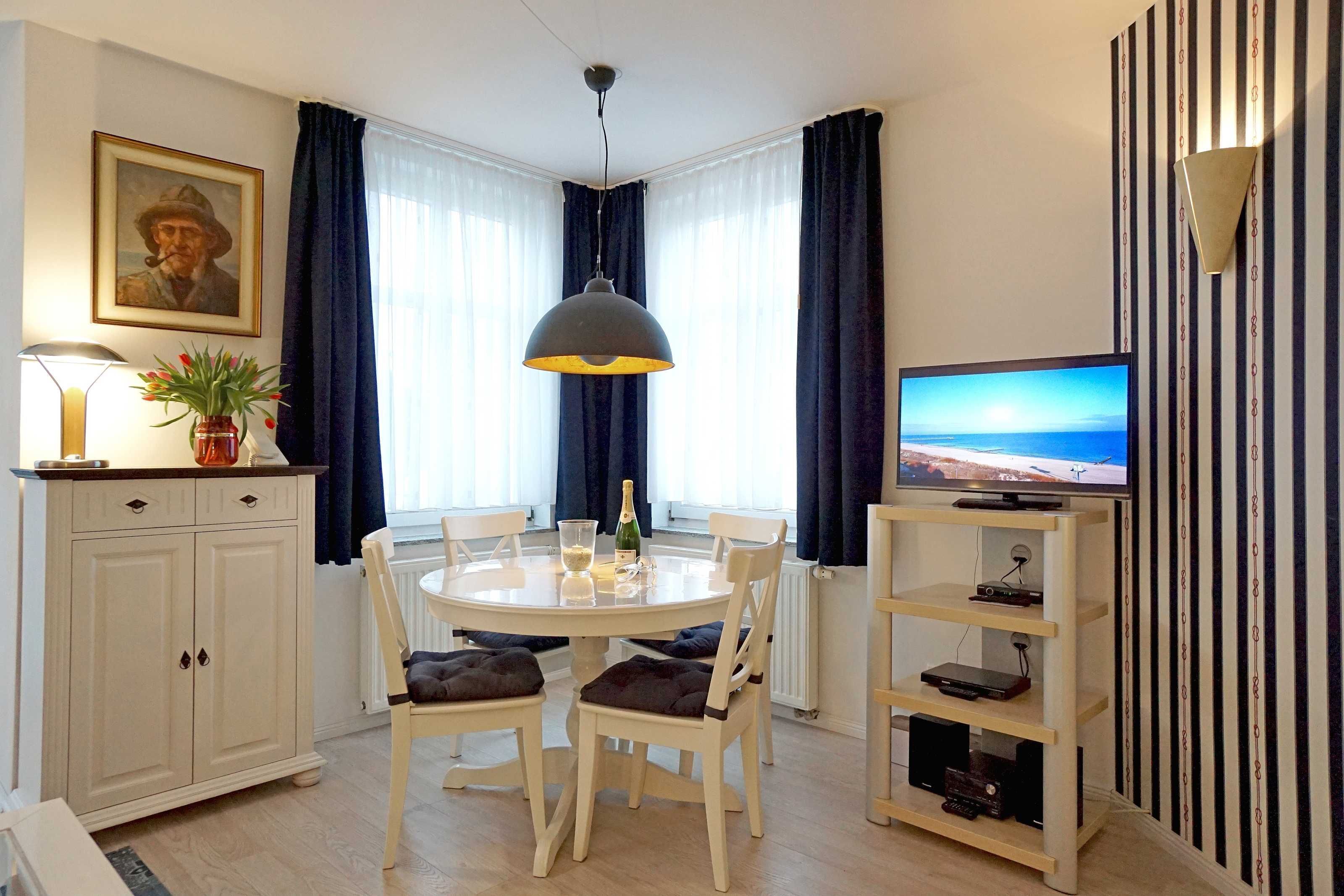Een eetruimte met een ronde tafel, stoelen, een kroonluchter, een televisie en een kast met een plant.