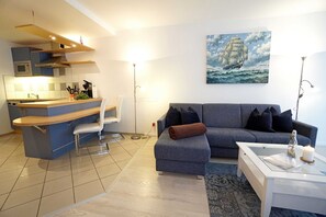 Ein modernes Wohnzimmer mit einer Küche, einem grauen Sofa, einem weißen Couchtisch und einem Gemälde eines Schiffes an der Wand.