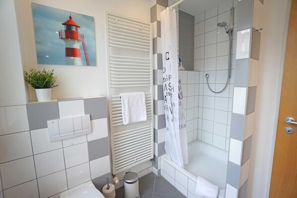 A modern bathroom with a shower, a towel rack, a potted plant, and a painting of a lighthouse.