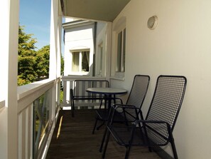 Un balcon avec une table et deux chaises, une balustrade blanche et une fenêtre avec un rideau.