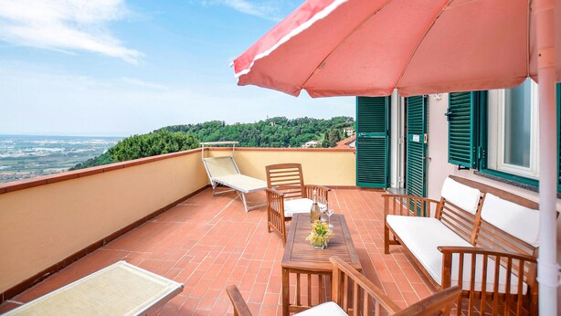 Ein Balkon mit Tisch und Stühlen, einem roten Sonnenschirm und Blick auf die Landschaft.