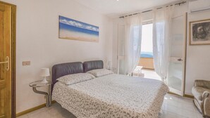 Ein Schlafzimmer mit einem Bett, einem Nachttisch, einem Fenster mit Vorhängen, einem Gemälde und einer Tür.