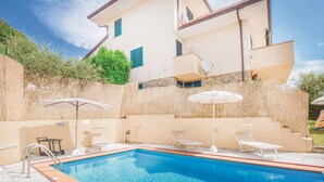 Ein Pool mit Liegestühlen und Sonnenschirmen, umgeben von einer Steinmauer und Bepflanzung.