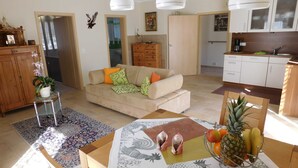 A living room with a sofa, coffee table, and a dining area with chairs and a fruit bowl. - Apartment am Rosengarten - Rosengarten (Füssen)