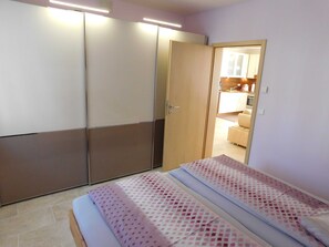 A bedroom with a bed, a wardrobe, and a kitchenette in the background. - Apartment am Rosengarten - Rosengarten (Füssen)