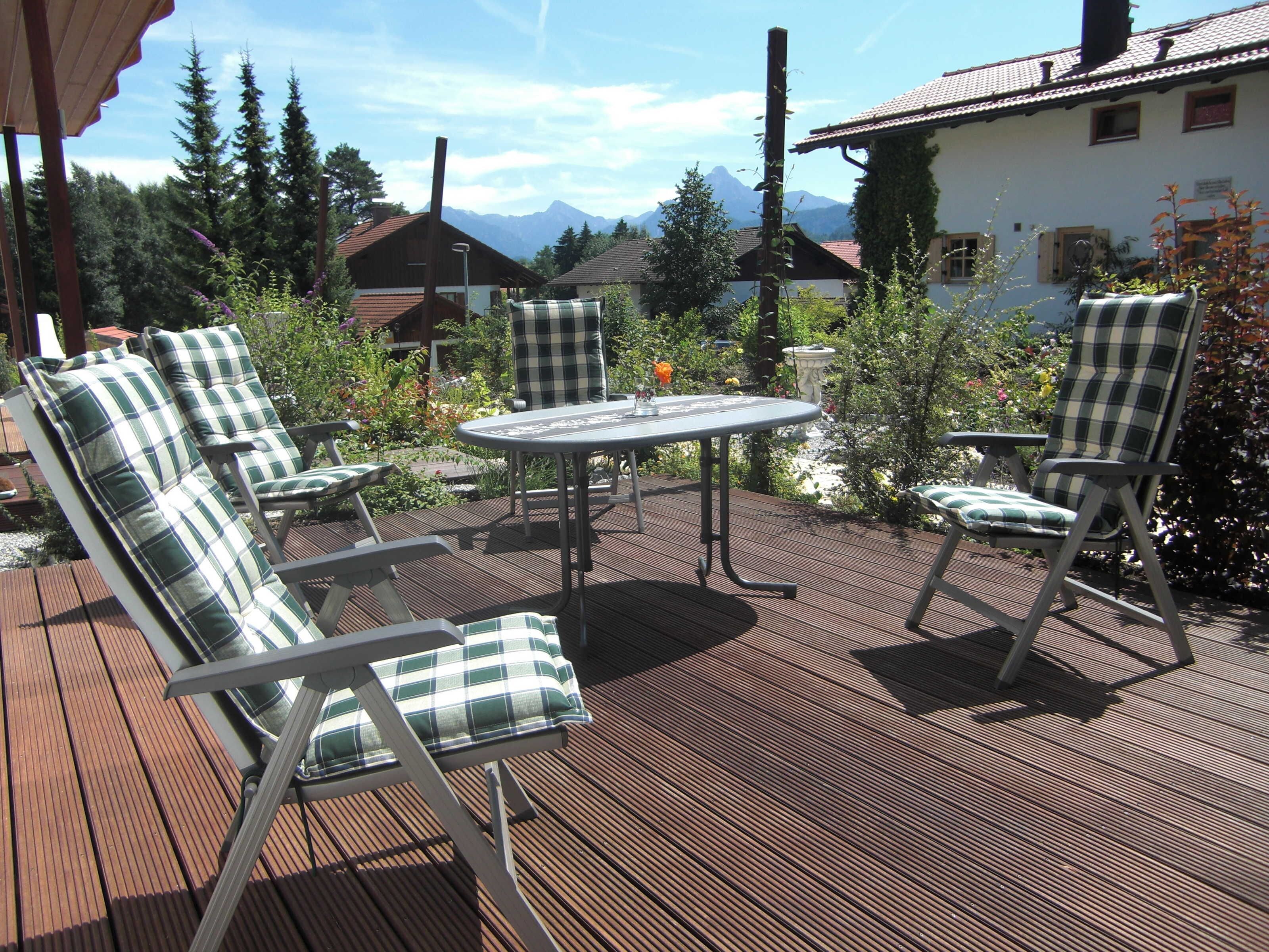 An outdoor patio with a table and four chairs, surrounded by greenery and a mountain view.