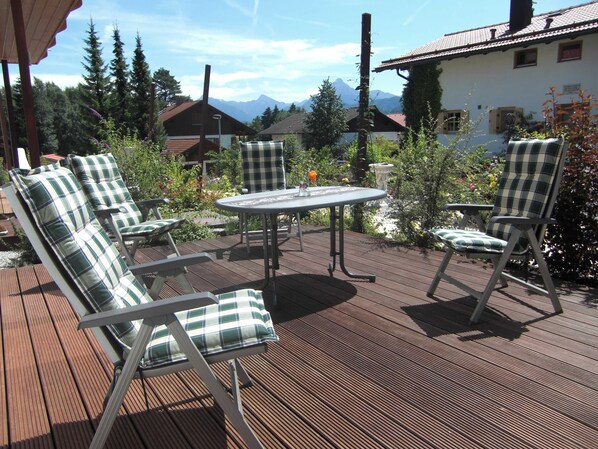 An outdoor patio with a table and four chairs, surrounded by greenery and a mountain view.