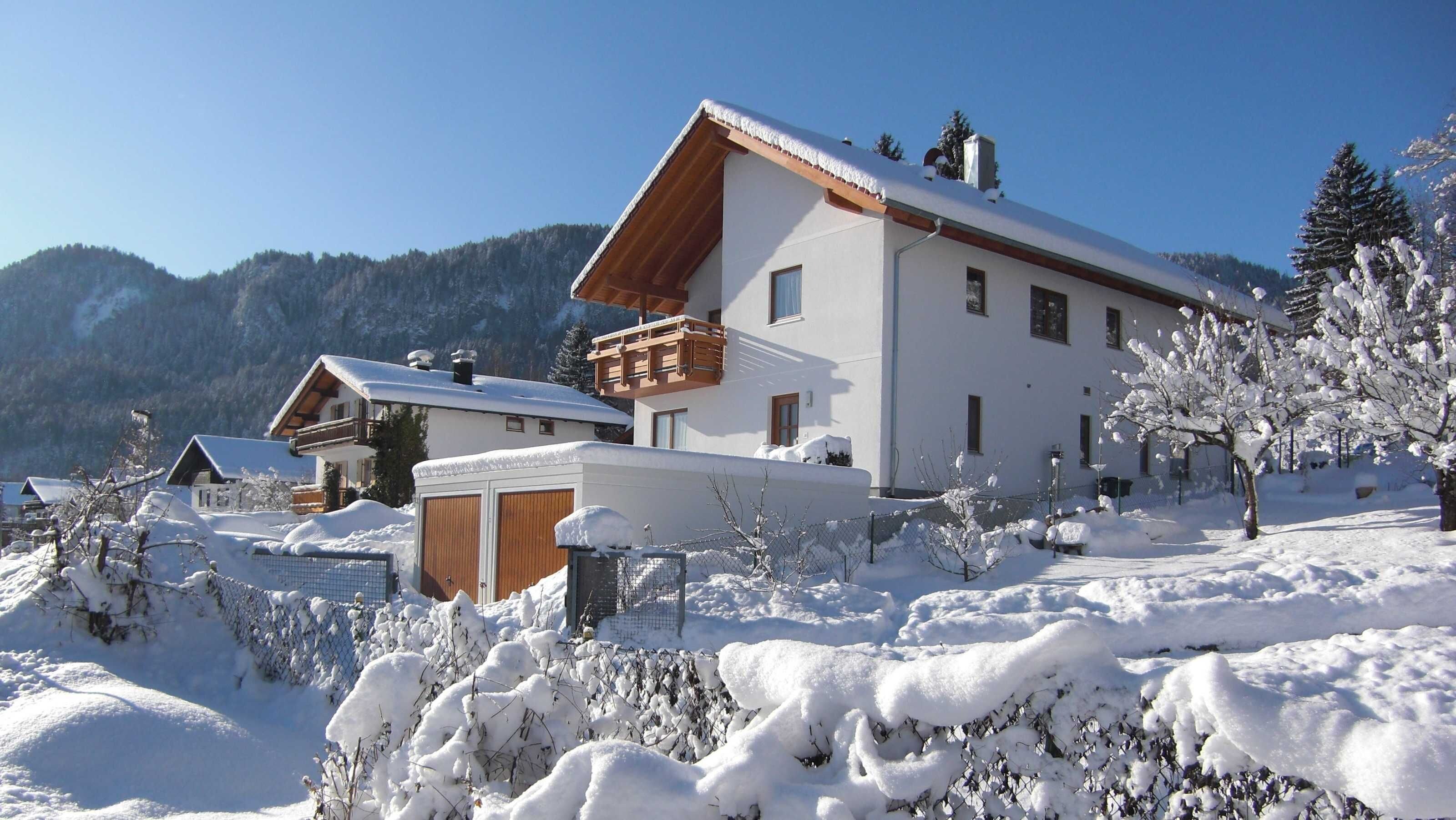 A snow-covered mountain resort with chalet-style buildings, wooden balconies, and a clear view of the surrounding mountains.