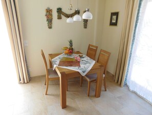 A dining area with a wooden table, chairs, a fruit bowl, and a decorative wall hanging.
