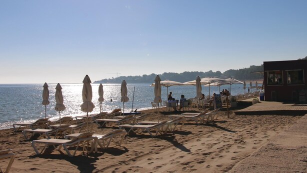 A beach with sun loungers and umbrellas, a clear sky, and a view of the water.