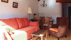 A cozy living room with a sofa, a wooden table, and a chair. There is a chandelier hanging from the ceiling and a lamp on the table.
