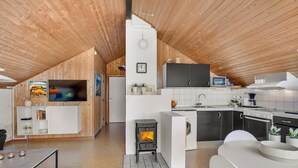 Een moderne keuken in loftstijl met een centraal houtgestookte kachel, witte kasten en een ingebouwde televisie.