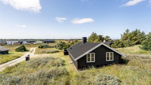 Een gelijkvloers blokhut met een donkere buitenkant, gelegen in een natuurlijke omgeving met gras en bomen.
