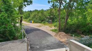 Un sendero pavimentado que atraviesa una zona boscosa, con una estructura de concreto a la izquierda y una cerca metálica a la derecha.