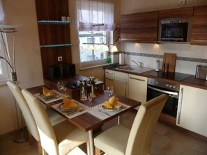 Une cuisine moderne avec des meubles en bois, un four à micro-ondes encastré et un coin repas avec une table dressée pour quatre personnes.