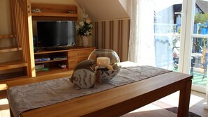 Un salon chaleureux avec un meuble TV en bois, un téléviseur à écran plat, un bol décoratif et une petite table avec un set de table.