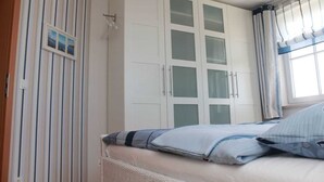 Une chambre à coucher avec un lit, une armoire aux portes vitrées, une fenêtre avec des rideaux et un mur à rayures.