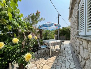 An outdoor patio with a table and chairs, a stone floor, and a garden with yellow flowers.