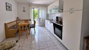 Een compacte keuken met witte kastjes, een eethoek met een bank en stoelen, en een kleine bank.