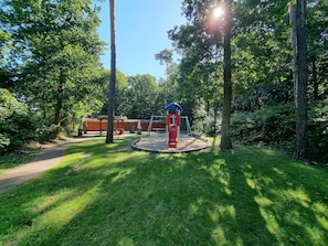 Un terrain de jeux avec des balançoires et un toboggan, entouré d’arbres et sous un ciel dégagé.