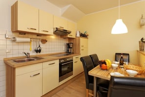 Une cuisine moderne avec des meubles en bois, un four encastré et un coin repas avec une table mise pour deux personnes.