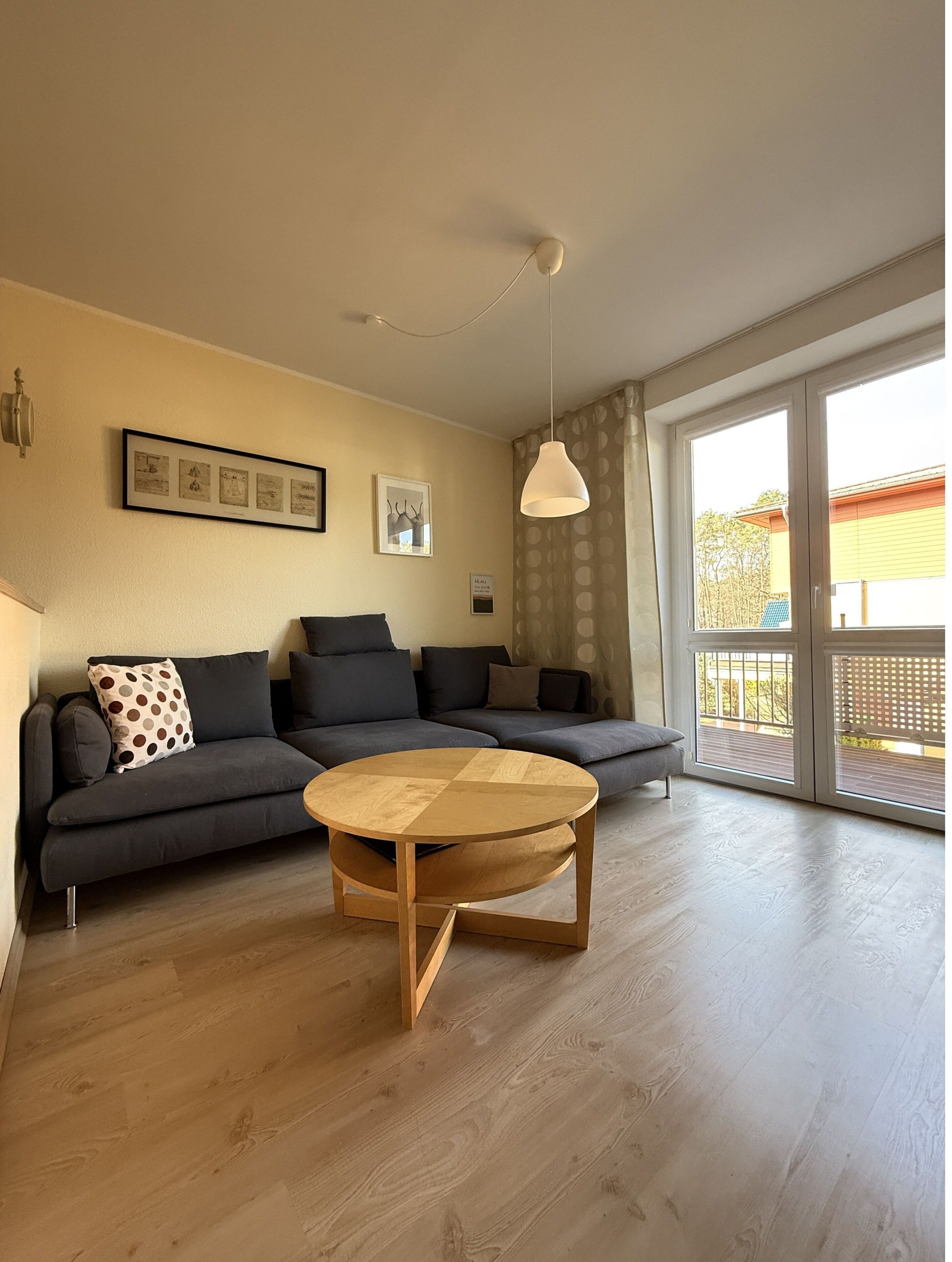 Een moderne woonkamer met een bank, een ronde houten salontafel en een plafondlamp.