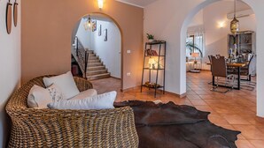 Un vaste espace de vie comprenant un canapé en osier, un tapis en cuir et un coin repas avec une table et des chaises.